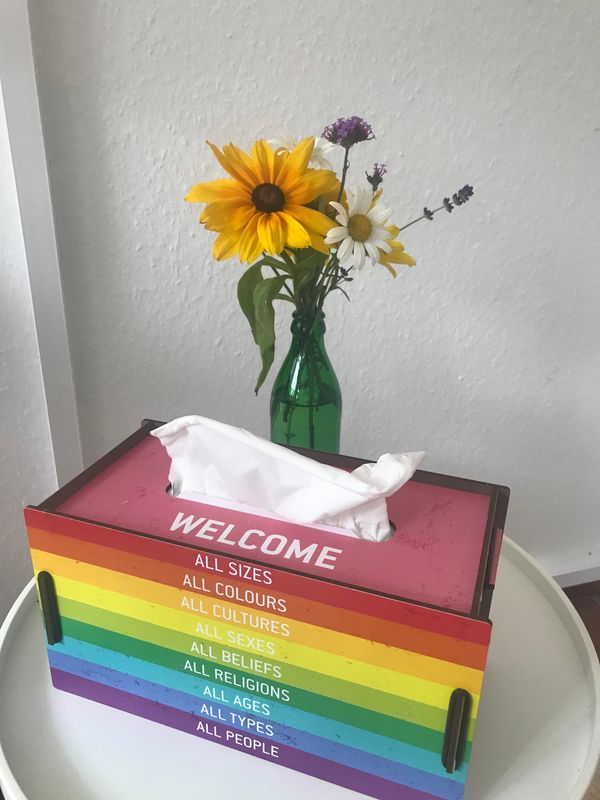 Taschentuchbox in Regenbogenfarben mit der Aufschrift Welcome und ein Blumenstrauß in der Beratungspraxis Die Krücke